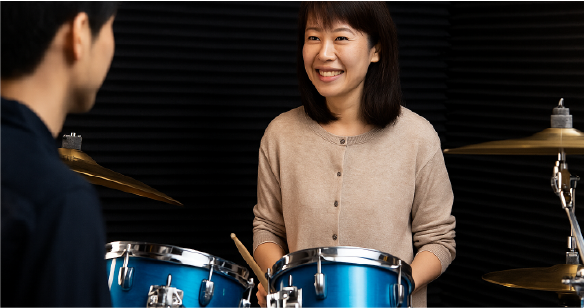 スタジオで40代女性が青いドラムを楽しそうに演奏している様子